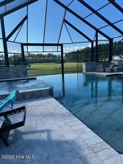 view of swimming pool with glass enclosure, a pool with connected hot tub, and a patio