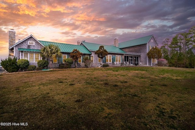 view of front facade with metal roof, a lawn, and a chimney