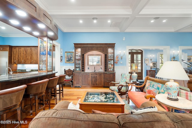 living room with beamed ceiling, a wainscoted wall, light wood-type flooring, wet bar, and coffered ceiling