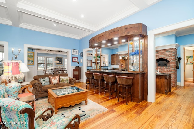 living area featuring wet bar, light wood-style flooring, beamed ceiling, and ornamental molding