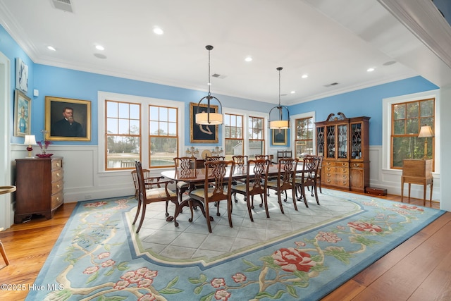 dining area featuring light wood-style floors, visible vents, a wealth of natural light, and wainscoting