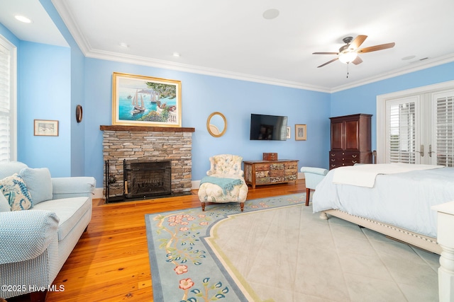 bedroom with a stone fireplace, wood finished floors, a ceiling fan, and ornamental molding