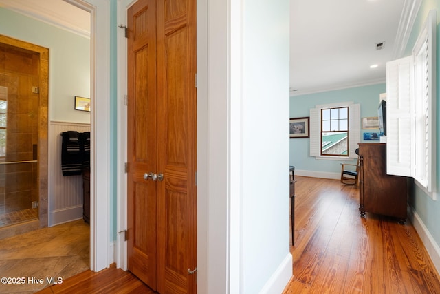 corridor featuring visible vents, baseboards, wood finished floors, and crown molding