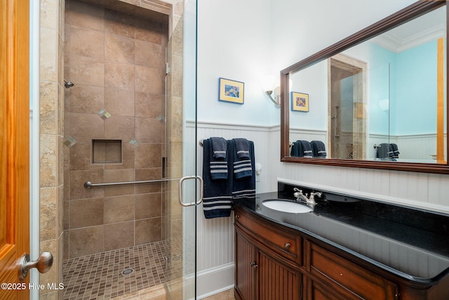 bathroom with wainscoting, a shower stall, vanity, and crown molding