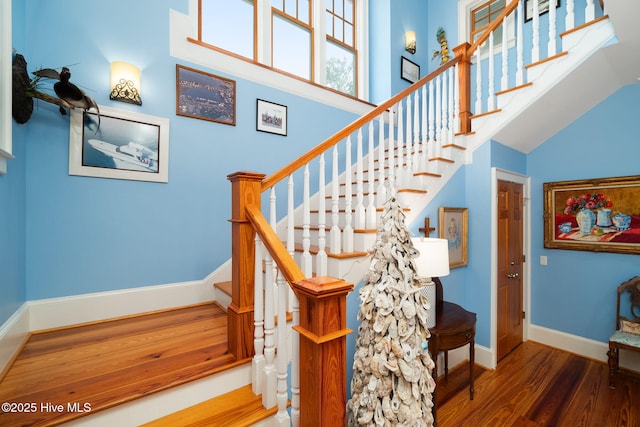 stairway with wood finished floors, baseboards, and a towering ceiling