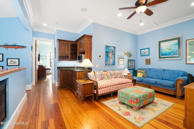 living room with visible vents, baseboards, light wood-style floors, and crown molding