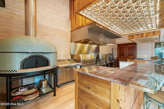 kitchen with premium range hood, light wood-style flooring, a peninsula, and wood walls