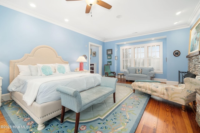 bedroom featuring a stone fireplace, wood finished floors, baseboards, and ornamental molding