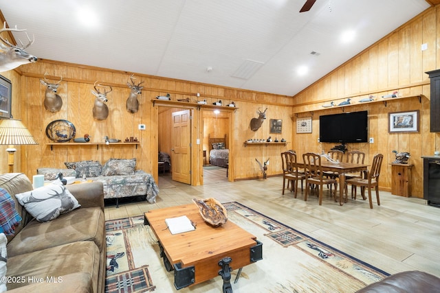 living room featuring wooden walls, visible vents, lofted ceiling, wood finished floors, and a ceiling fan