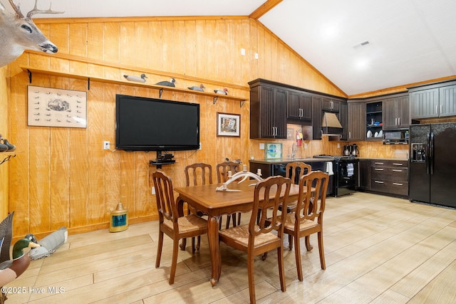 dining room with light wood-type flooring, wooden walls, visible vents, and high vaulted ceiling