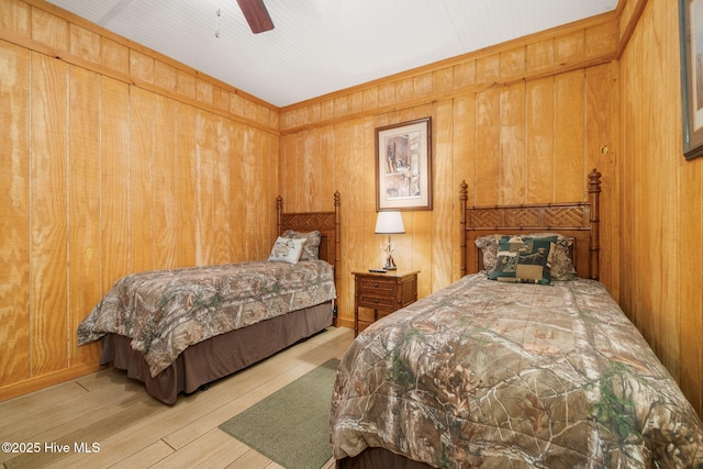 bedroom with a ceiling fan, wooden walls, and wood finished floors