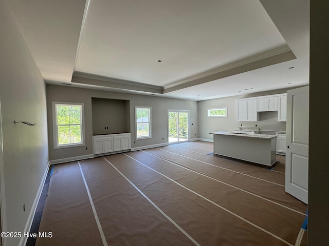 unfurnished living room with a raised ceiling, baseboards, and a wealth of natural light