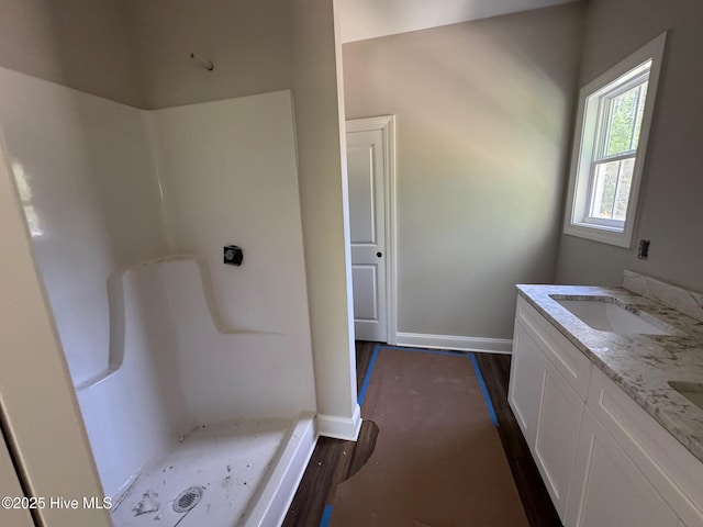 bathroom featuring a sink, double vanity, baseboards, wood finished floors, and a shower