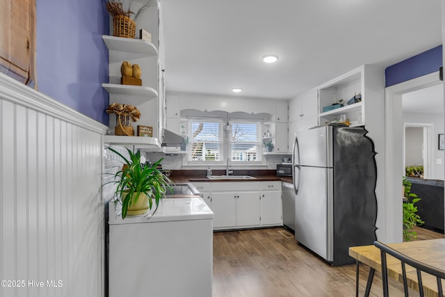 kitchen with tasteful backsplash, white cabinetry, sink, stainless steel appliances, and light hardwood / wood-style flooring