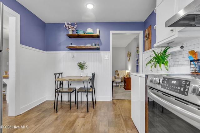 kitchen featuring extractor fan, stainless steel electric range oven, light wood-type flooring, decorative backsplash, and white cabinets