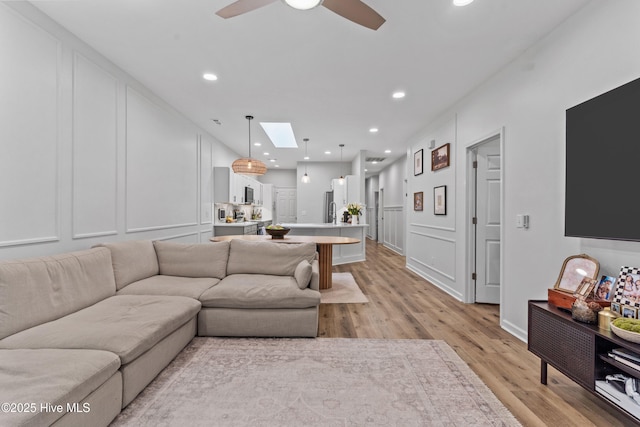 living room with a skylight, light hardwood / wood-style floors, and ceiling fan