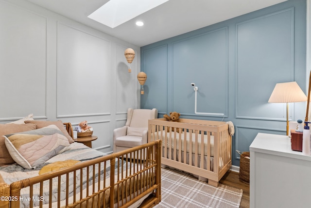 bedroom with a nursery area, wood-type flooring, and a skylight