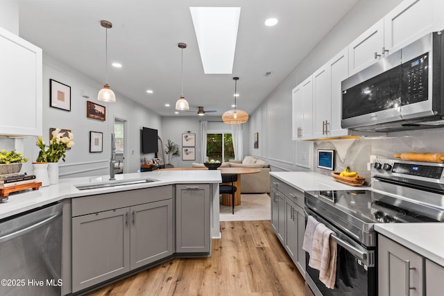 kitchen with decorative light fixtures, a skylight, light hardwood / wood-style flooring, appliances with stainless steel finishes, and gray cabinets