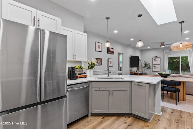 kitchen with pendant lighting, sink, gray cabinetry, a skylight, and stainless steel appliances