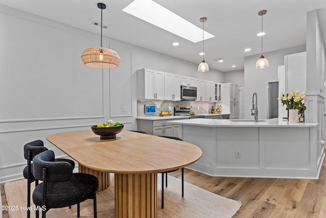 kitchen featuring appliances with stainless steel finishes, decorative light fixtures, a skylight, sink, and white cabinets