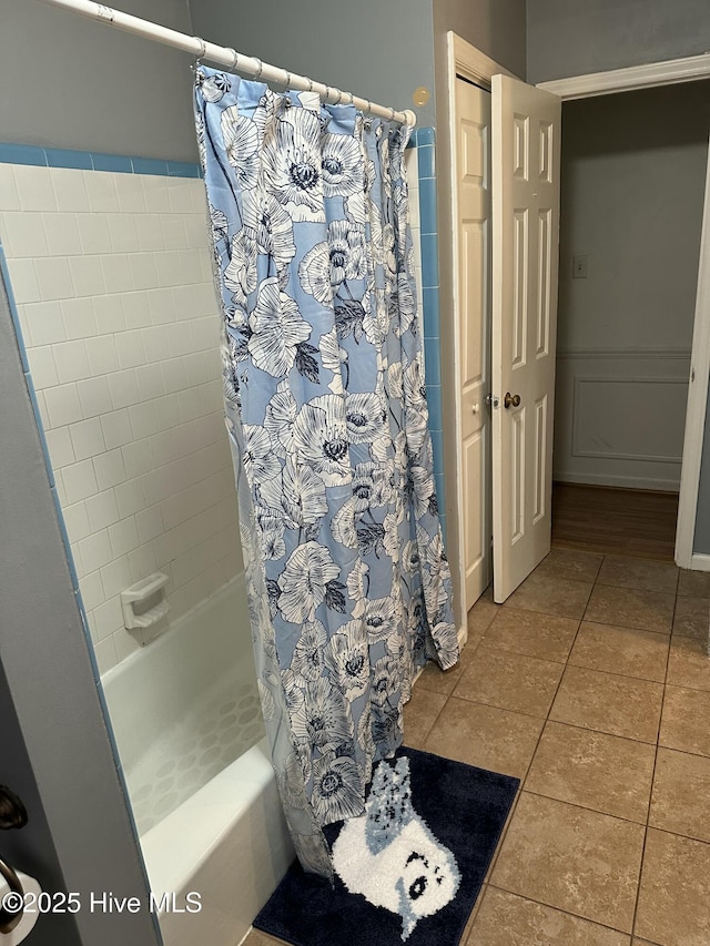 bathroom with tile patterned flooring, shower / tub combo, and a wainscoted wall