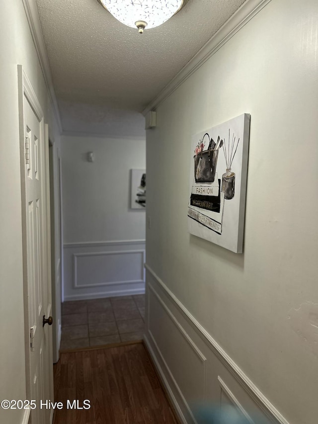 hall featuring a wainscoted wall, ornamental molding, a textured ceiling, a decorative wall, and dark wood-style flooring