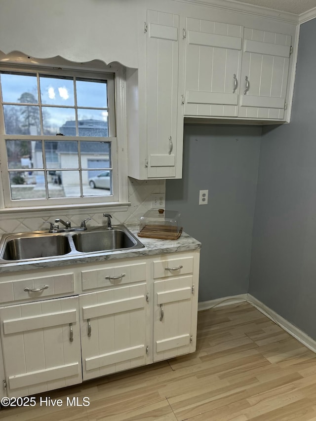 kitchen with baseboards, light countertops, light wood-type flooring, white cabinets, and a sink