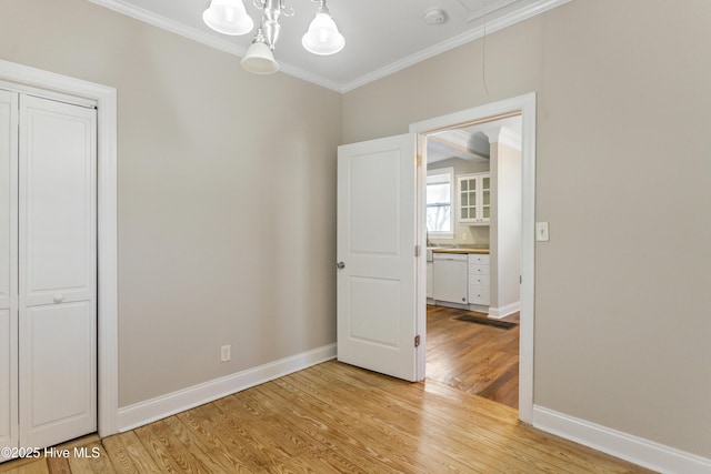 unfurnished room with crown molding, baseboards, attic access, and light wood finished floors