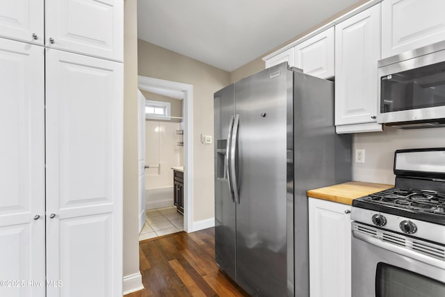kitchen with appliances with stainless steel finishes, baseboards, white cabinets, dark wood-style floors, and butcher block counters