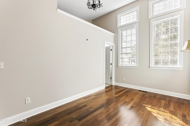 unfurnished room featuring a notable chandelier, baseboards, visible vents, and wood finished floors
