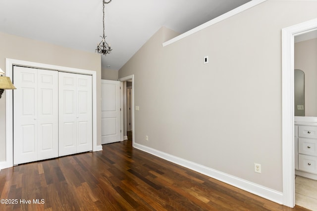 unfurnished bedroom featuring dark wood-style floors, a closet, an inviting chandelier, baseboards, and vaulted ceiling