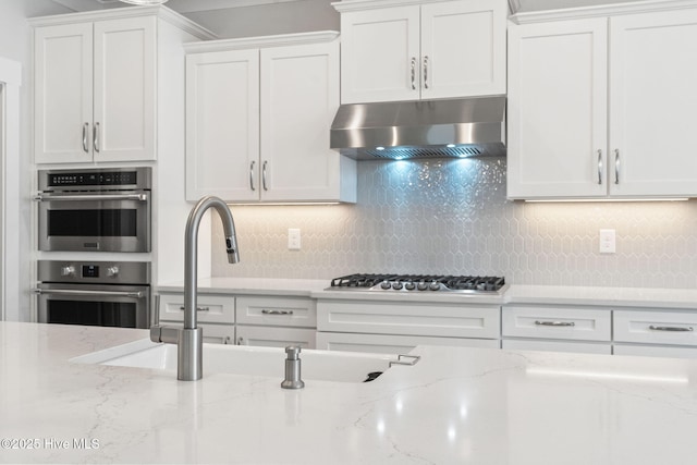 3836 Mason Port Dr, Wilmington, NC 28409 - kitchen with wall chimney range hood, stainless steel appliances, white cabinets, tasteful backsplash, and light stone counters
