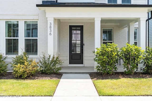 3836 Mason Port Dr, Wilmington, NC 28409 - doorway to property featuring brick siding, a porch, and a lawn