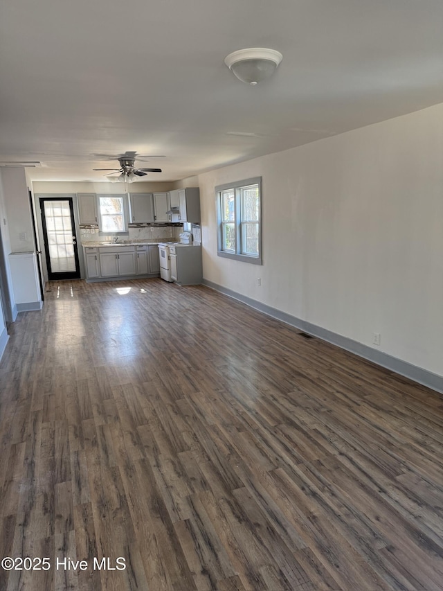 unfurnished living room with plenty of natural light, dark wood-type flooring, and ceiling fan