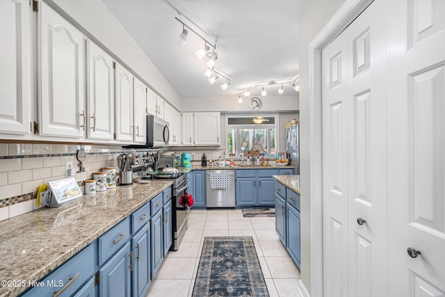 kitchen featuring appliances with stainless steel finishes, blue cabinetry, light tile patterned floors, and white cabinets