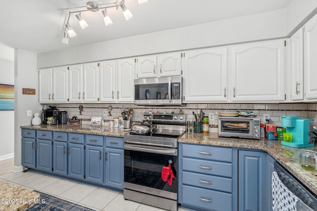 kitchen featuring appliances with stainless steel finishes, blue cabinets, white cabinetry, decorative backsplash, and light tile patterned floors