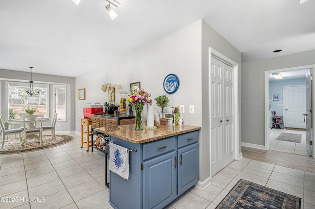 kitchen featuring pendant lighting, blue cabinetry, an inviting chandelier, light stone counters, and light tile patterned flooring