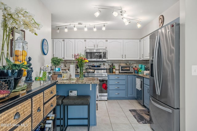 kitchen with stainless steel appliances, tasteful backsplash, white cabinets, blue cabinets, and light tile patterned flooring