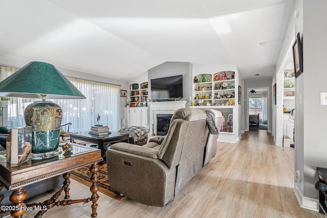 living room featuring vaulted ceiling, built in features, and light hardwood / wood-style flooring