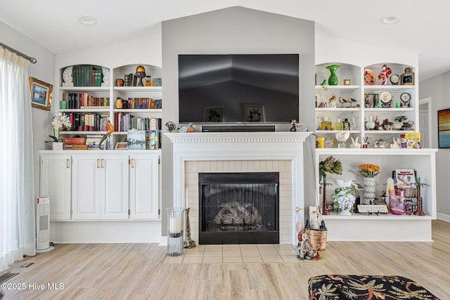 living room featuring vaulted ceiling, built in features, and light hardwood / wood-style flooring