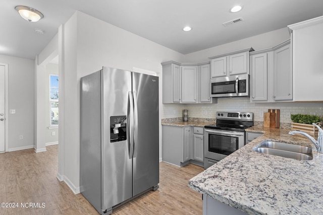 kitchen featuring sink, gray cabinets, stainless steel appliances, light hardwood / wood-style floors, and backsplash