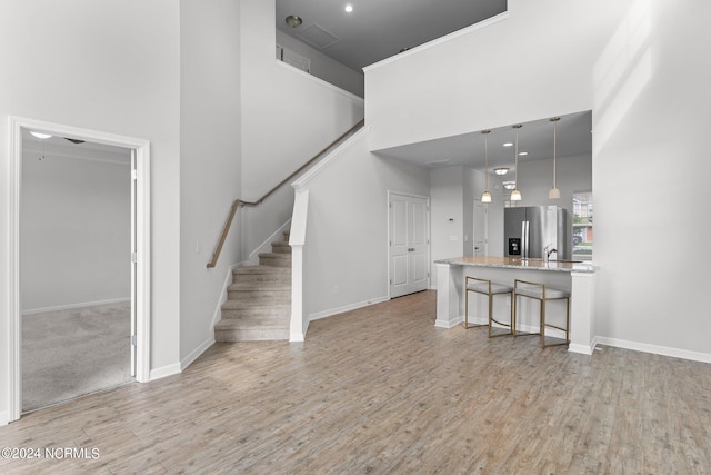 unfurnished living room with a towering ceiling, sink, and light hardwood / wood-style floors