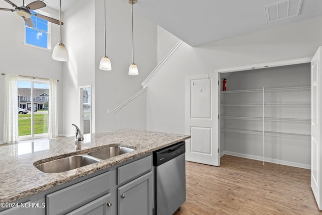 kitchen with sink, decorative light fixtures, stainless steel dishwasher, light stone countertops, and light hardwood / wood-style floors