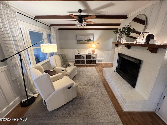 living room featuring crown molding, dark wood-type flooring, ceiling fan, a brick fireplace, and beamed ceiling