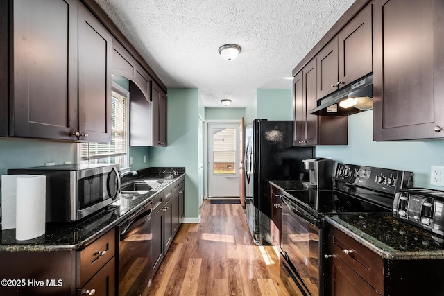 kitchen featuring light wood-type flooring, dark stone countertops, black appliances, and dark brown cabinets