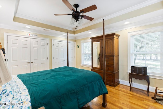 bedroom with ornamental molding, two closets, light hardwood / wood-style floors, and a tray ceiling