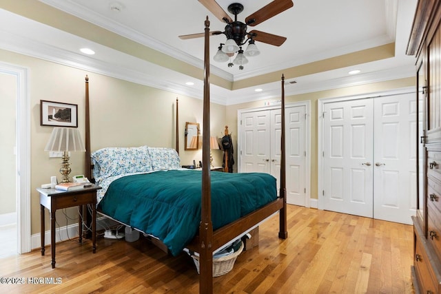 bedroom featuring light hardwood / wood-style flooring, ornamental molding, a raised ceiling, and multiple closets