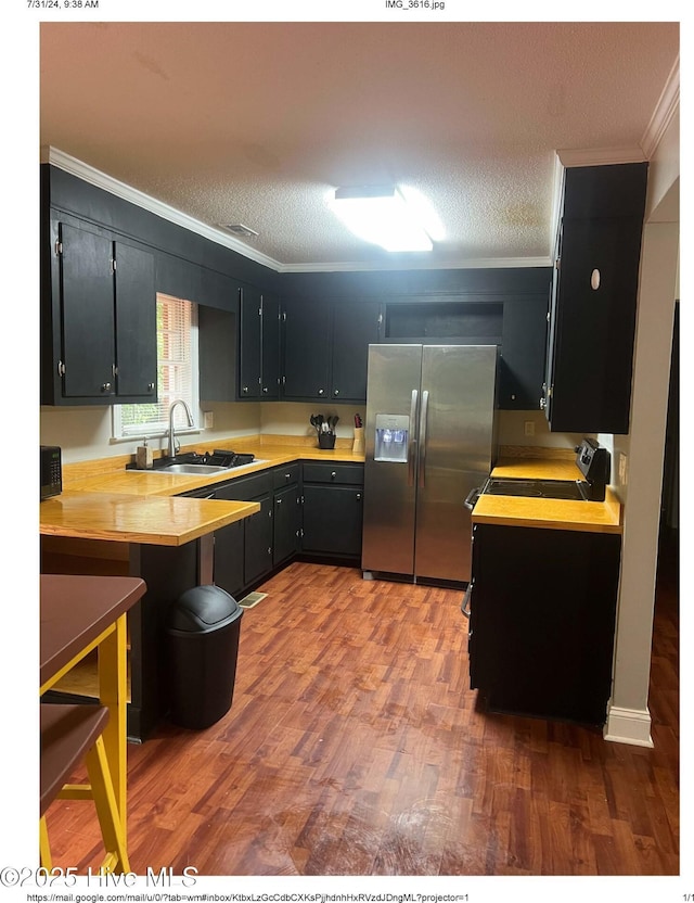 kitchen with stainless steel refrigerator with ice dispenser, ornamental molding, sink, and a textured ceiling