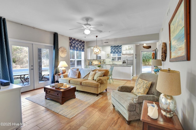 living room with french doors, ceiling fan, and light wood-type flooring