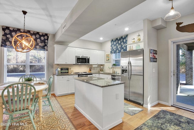 kitchen with a center island, dark stone counters, pendant lighting, stainless steel appliances, and white cabinets